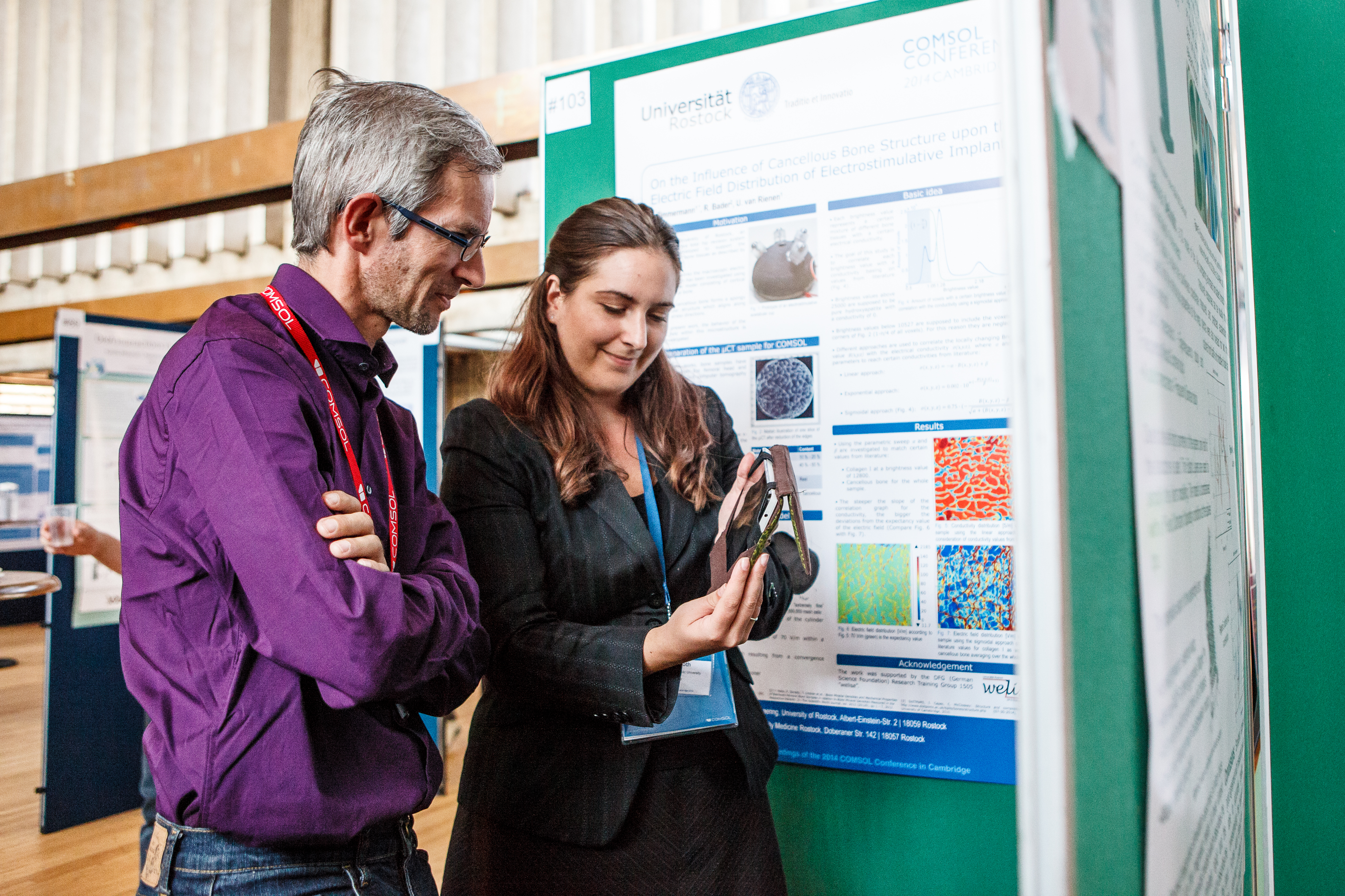 Two COMSOL Conference attendees in the exhibition hall, where one is presenting their work.